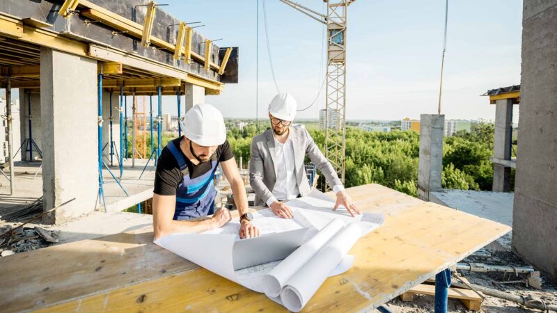 Contractor and project manager reviewing plans on site, highlighting business insurance for construction companies.